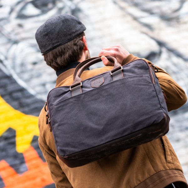 Mann hält Buisnesstasche Laptoptasche aus gewachster Baumwolle mit Lederelementen in schwarz über der Schulter